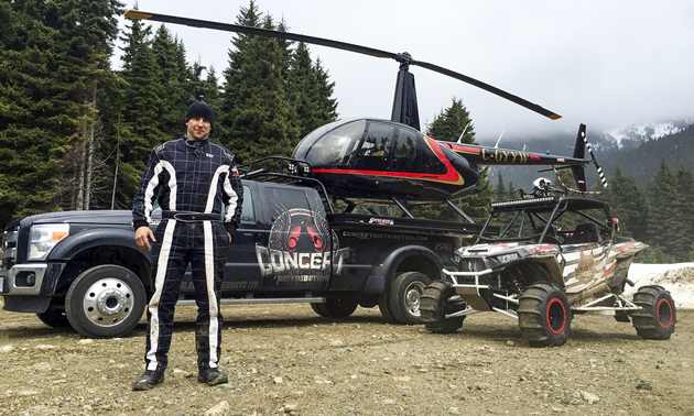 Al McBeth standing beside a truck with a helicopter on it and a custom Polaris RZR side by side. 