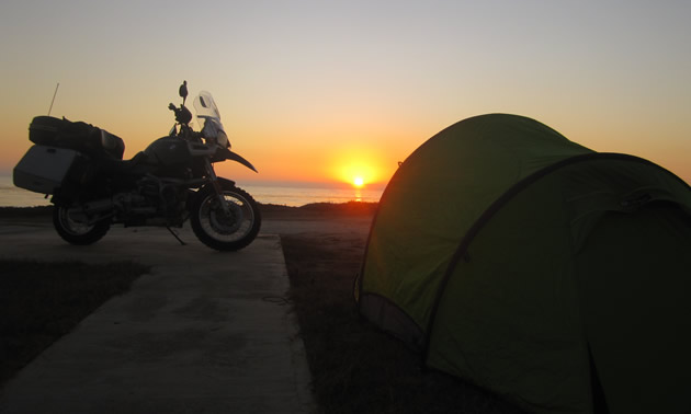 Photo of a bike on a concrete pad beside a yellow tent with the sunset in the background.