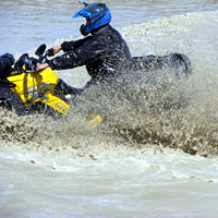 An ATVer riding through a deep mud pit. 