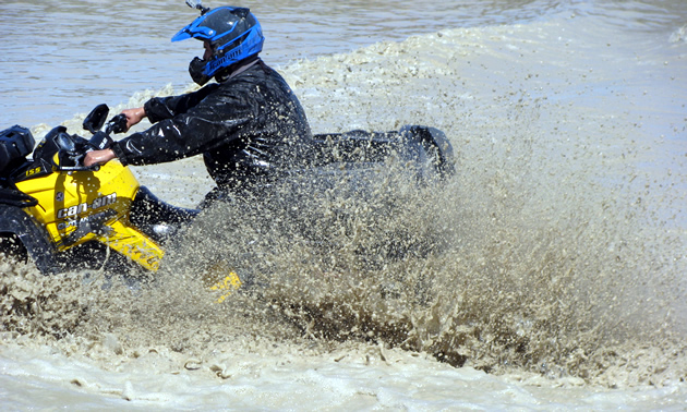 An ATVer riding through a deep mud pit. 