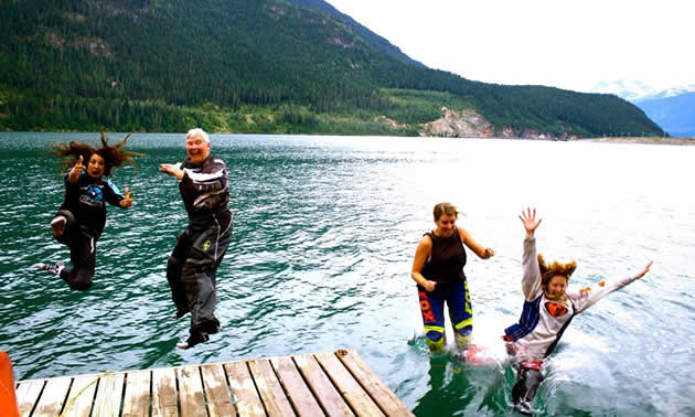 A group jumps into the lake with full moto gear on. 