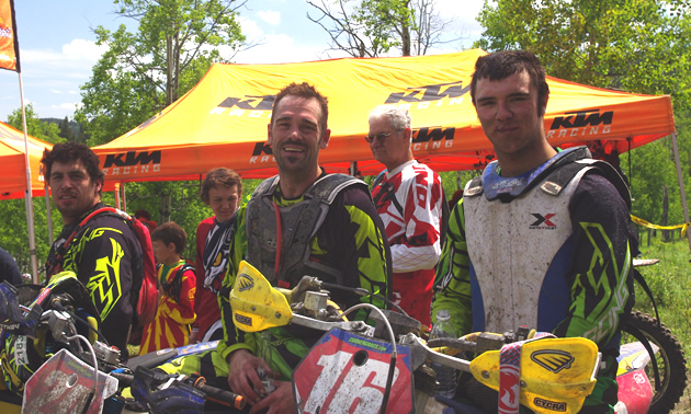 Three men sitting on dirt bikes after a race. 