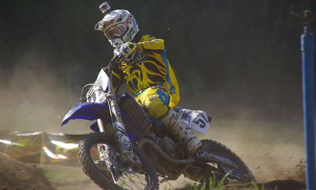 Photo of a young man dressed in yellow riding gear on a blue dirt bike. 