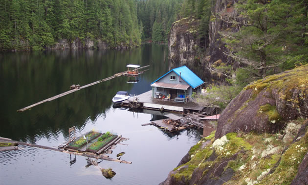 A small floating cabin on the lake with granite cliffs sheltering it. 