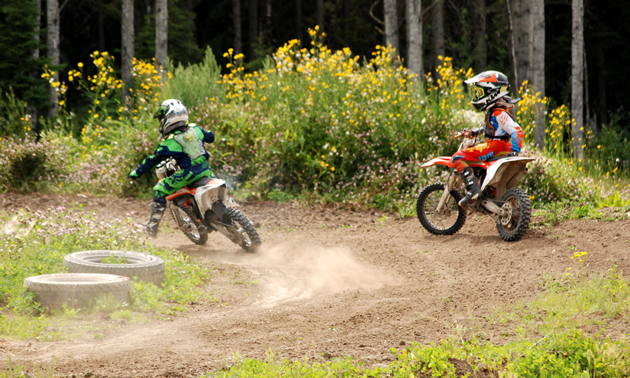 One young rider watches another practice laps on the motocross track. 