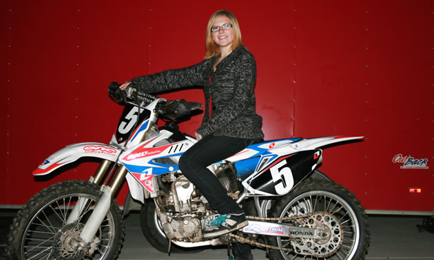 A blonde teenager leaning against her dirt bike