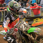 Guy on a green dirt bike leaning into a corner on a dirt track with the crowd in the background.