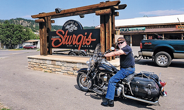 A man sitting on a Harley in front of the Sturgis sign. 