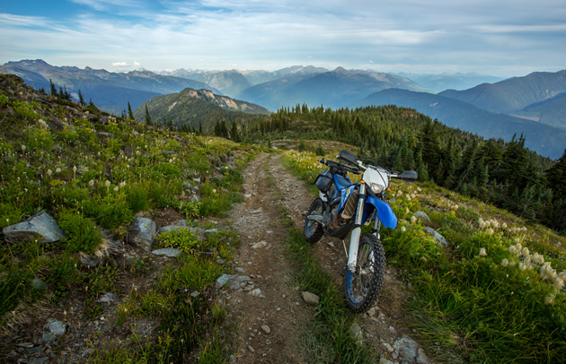 A dirt bike parked alone a mountain trail. 