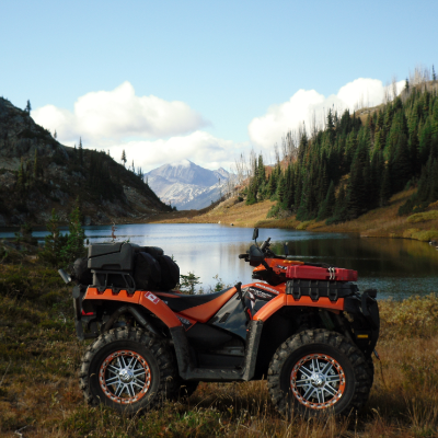 An ATV idles near a lake and mountains. 