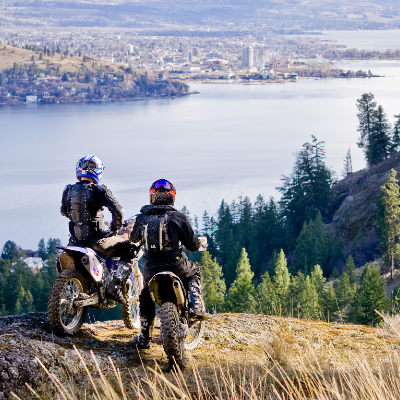 Two dirt bikers look over a river in a valley.