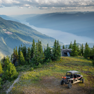An ATV is parked on a green mountaintop. Another mountain and a river are in the background.