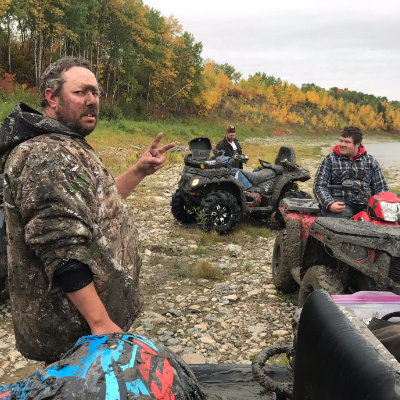 A muddy Chad Taylor gives the peace sign while his friends Matt and Brendan take a break on their ATVs
