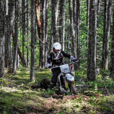 Kitt Stringer riding a dirt bike in a dense forest at the Kirk
