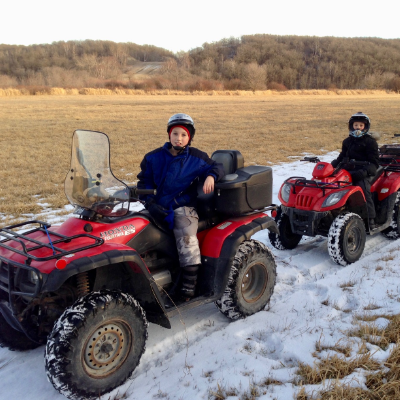 Three ATVs are lined along a snow-covered trail in an open field.
