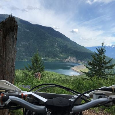 A beautiful view of mountains and a lake from behind the handlebars of a dirt bike.