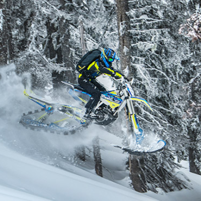 A blue and yellow snow bike gets powdered air through frosty trees.