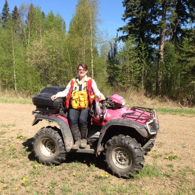 Trina Tosh wears a safety vest while sitting on a red ATV on a trail