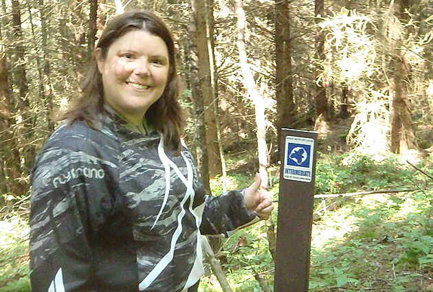 A brown-haired woman standing by a sign post with a terrain rating on it. 