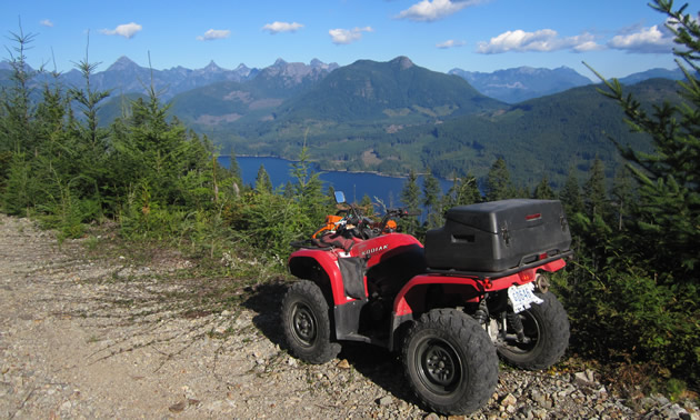 A red ATV parked on the side of a logging road overlooking Powell Lake. 