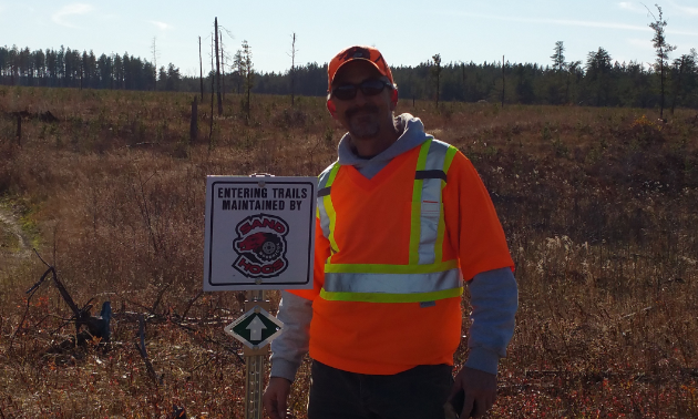 Gary Hora is standing beside signage for one of the trails maintained by the Woodridge Sandhogs.
