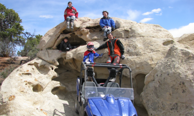 A family poses happily in front of a side-by-side on some large rocks in Richfield, Utah.