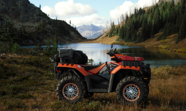 An ATV idles near a lake and mountains. 