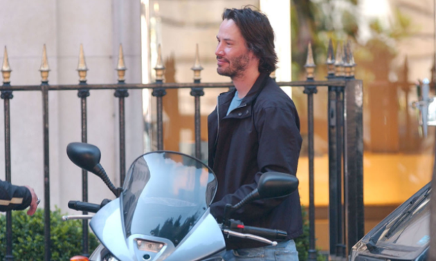 Keanu Reeves smiles as he prepares to ride his motorcycle. 