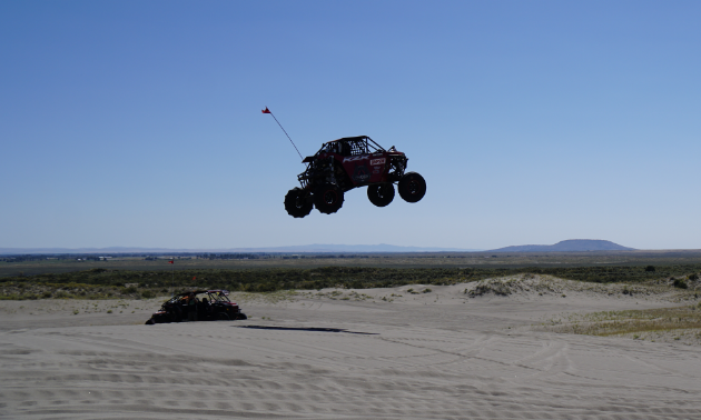A UTV leaps up above the horizon from a dune in a desert.