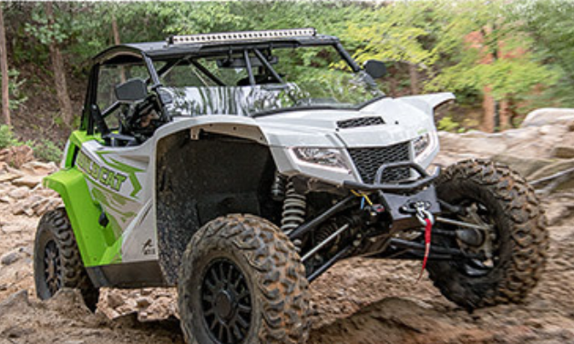 A 2021 Arctic Cat side-by-side climbs over rocky terrain. 