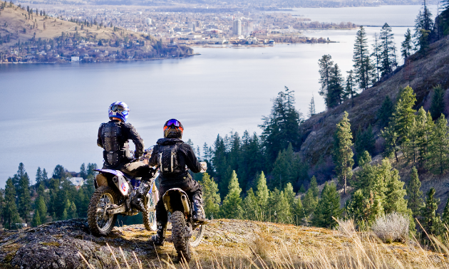 Two dirt bikers look over a river in a valley.