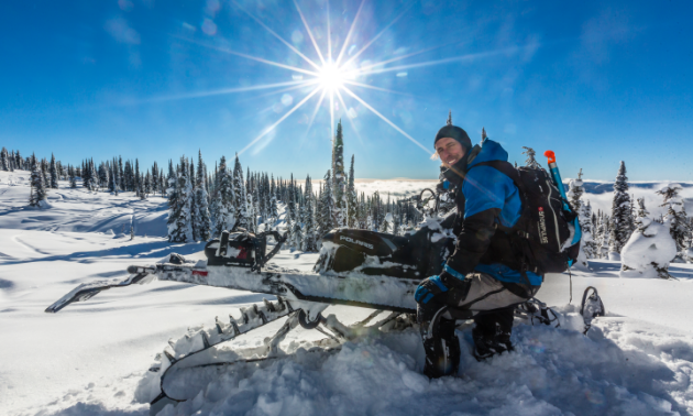Billy Stevens smiles for the photo while leaning against his snowmobile in the snowy mountains.