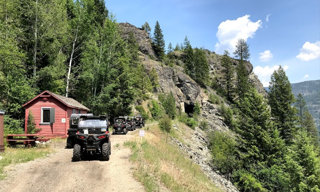 A row of ATVers ride along a trail on a mountainside. 
