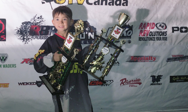 Aiden Lawrence poses with two giant trophies that nearly match him in size.