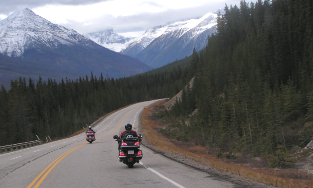 Motorcyclists ride down a road through the mountains.