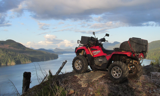 An ATV sits on the crest of a cliff overlooking a lake.