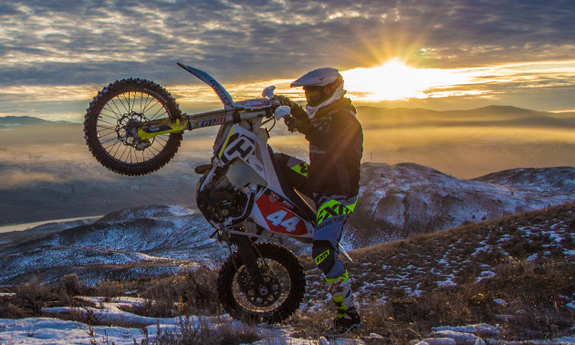 Dustin Labby does a wheelie while the sun breaks through the clouds behind him.