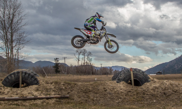 Dustin Labby gets big air as he jumps off of big tires in a field.