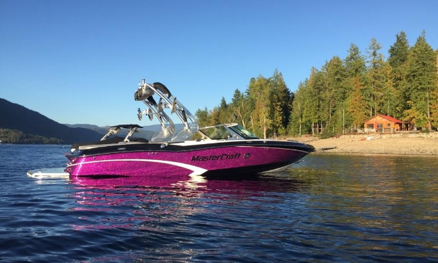 A purple wakeboarding boat idles on a lake.