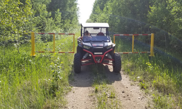 An ATV is parked near a gate on a trail in the woods.