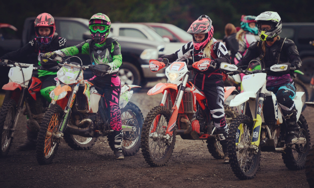 A row of four dirt bikers lined up next to each other.