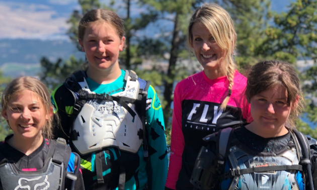 A woman and her three girls wearing motocross gear.