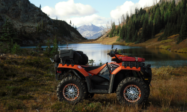 An ATV is parked beside a lake with a mountain protruding in the distance.