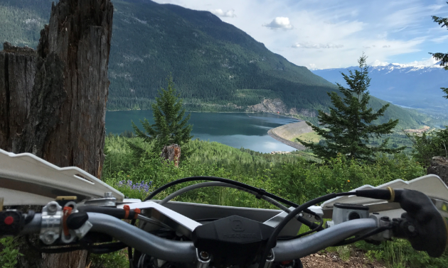 A beautiful view of mountains and a lake from behind the handlebars of a dirt bike.