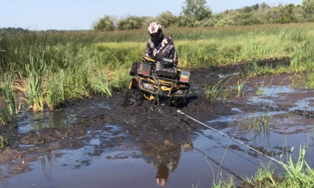 Ryan Ruf is stuck in deep mud. A wench is tied to something out of view to pull his ATV out.