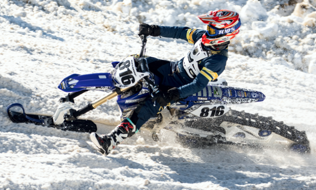 A blue and white snow bike leans into a tight turn. 