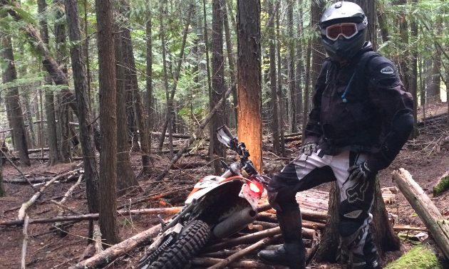 Shawn Handley stands next to his motorcycle in the woods.