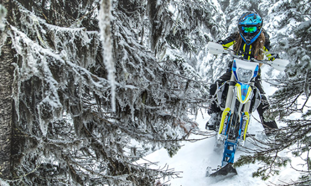 A blue and yellow snow bike makes its way through snow-covered trees.