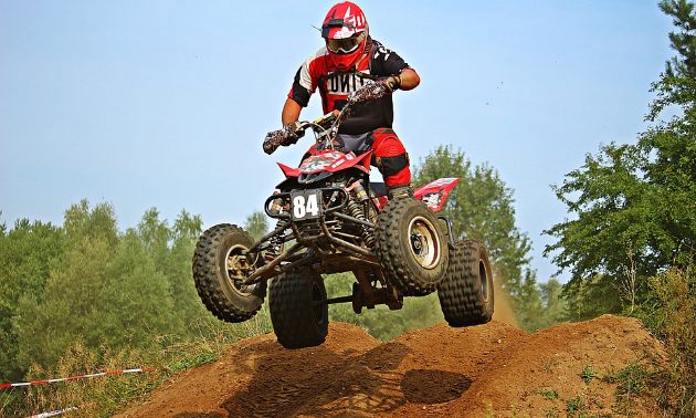 An ATV rider gets air over a dusty jump.