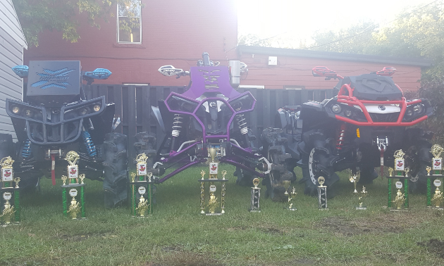 A line of trophies sits in front of 3 ATVs